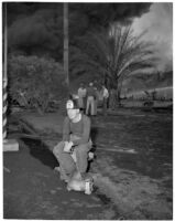 Fire fighter taking a break while smoke rises over L.A. Harbor in the background, coming from fires caused by the Markay oil tanker explosion, Los Angeles, 1947