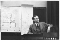 Murder suspect Robert S. James sitting on the witness stand with a map of his house behind him, Los Angeles, 1936