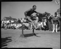 Jesse Owens jumps over a hurdle while spectators watch from the sideline, Los Angeles, 1930s