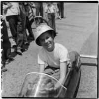 Al Pedrosa smiling in his soap box derby car while a crowd gathers for the race, Los Angeles, 1946