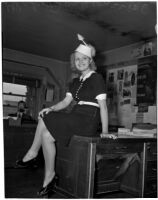 Gladys Jackson sits on a desk wearing a dress and hat, Los Angeles, 1930s