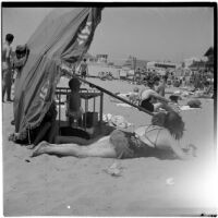 Two woman and a baby in a crib under an umbrella at the beach on Labor Day, Los Angeles, September 3, 1945