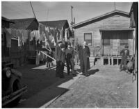 Four well-dressed men stand together in the Los Angeles slums while a fifth man looks on, Los Angeles, 1925-1945