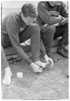 USC track athlete taping his foot on the sidelines at a meet, Los Angeles, 1937