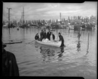 Unidentified men and women carry belongings and pets across flood waters, Long Beach, circa 1930s