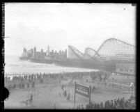 Roller coaster and buildings along pier with beach goers on shoreline of beach of on Santa Monica Pier, Santa Monica, circa 1923