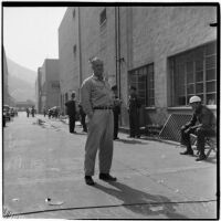 Walter Bush stands outside of a guarded building, Los Angeles, 1930s