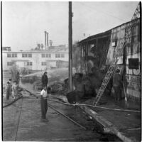 Fire fighters hose down a hay barn fire as children gather to watch, Los Angeles, 1945