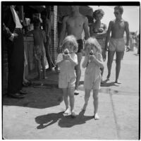 Two young girls in matching overalls eat snow cones on Labor Day, Los Angeles, September 3, 1945