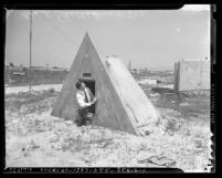 Man sitting in doorway of concrete, triangle shaped bomb shelter in Los Angeles, Calif., circa 1941