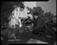 Clifford E. Clinton in a bathrobe investigating a hole in the wall of a house with police officer J.E. Hermans, Los Angeles