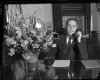 Supervisor John Anson Ford sits at his desk at the Hall of Records with a bouquet of flowers, Los Angeles, 1930s