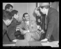 Actor Clark Gable seated, surrounded by group of five men, circa 1937