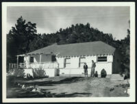 Aldous and Maria Huxley standing in front of Huxley house, Wrightwood CA [descriptive]