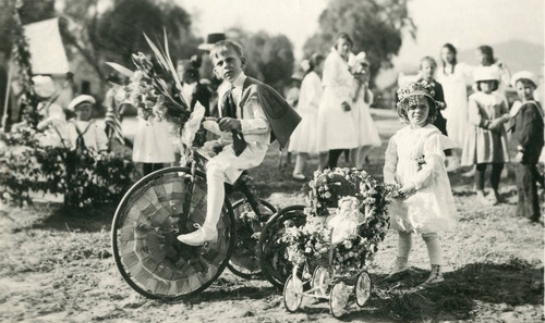 George and Carolyn Barker with bicycle and doll carriage during the ""Children's Floral Parade"" in Banning, California