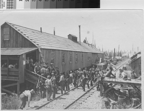 [Workers assembling near building next to railroad tracks]