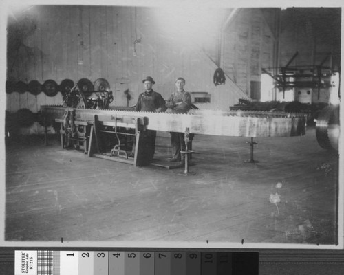 [Two men posed in center of large band saw]