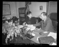 Actress Anna May Wong sitting at desk with Los Angeles District Attorney Buron Fitts reviewing extortion letters, Los Angeles, 1937