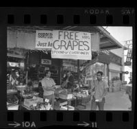 Produce market offering free grapes while picket with sign stating "Support Grape Boycott" walks past in Los Angeles, Calif., 1969