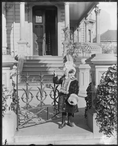 Anita Oliver as child, standing at gate. [negative]