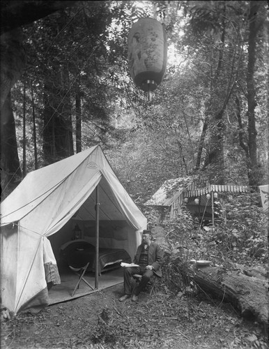 Man seated in folding chair outside tent, Bohemian Grove. [negative]