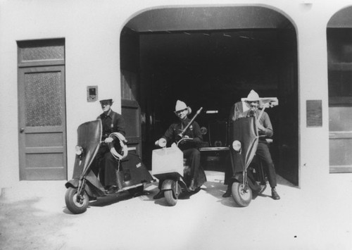 Ira Wisner, Floyd Higgins, and George Horton on motor scooters in front of Orange Fire Station on Olive Street, Orange, California, ca. 1950