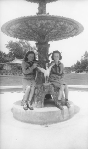 Two Girl Scouts sitting on the original Plaza fountain after its move to Orange City Park, Orange, California, 1944