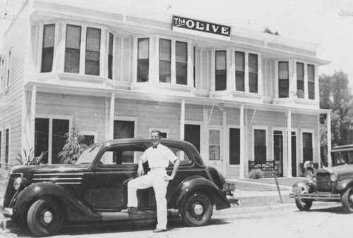 Owen McDiel standing by 1936 Ford in front of Olive Hotel, Olive, California, 1938