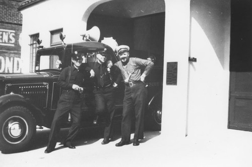 Ira Wisner, Floyd Higgins, and George Horton lean against fire rescue truck in front of Orange Fire Station on Olive Street, Orange, California, ca. 1950