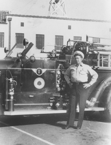 Floyd Higgins standing next to Orange Fire Truck No. 1 in front of South Olive Street fire station, Orange, California