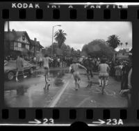 Three male streakers running and cycling through rain at USC as crowd watches, Los Angeles, Calif., 1974
