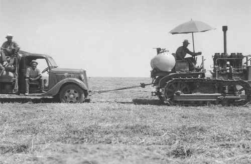 Tractor pulling truck out of a sandy field