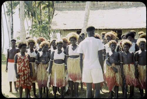 Group of dancers in grass skirts and matching headress; some with western dress or tops