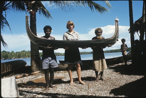 Frances Harwood and two men holding a miniature canoe