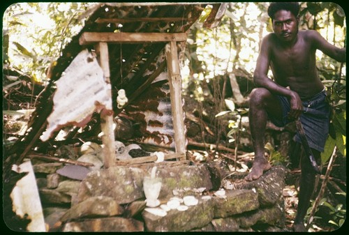 Man with shrine with shelter, skulls, shell jewelry, mortar and pestle