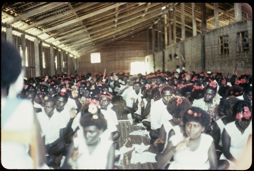 Church with seated group; wearing white clothing and red flowers in hair