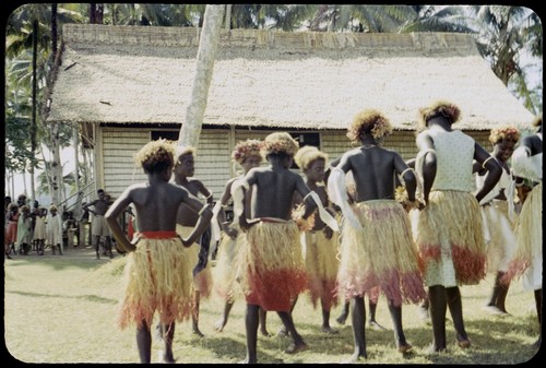 Dancers in grass skirts and matching headress; some with western dress or tops