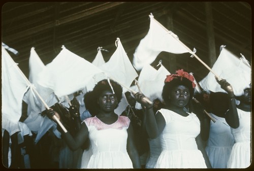 Girls dressed in white and holding white flags inside a building