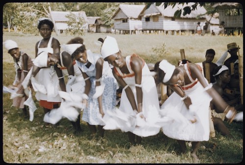 Dancers in white dresses with red trim; musicians in background