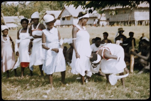 Dancers in white dresses with red trim, with musicians in background