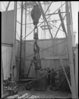 Four men standing next to the travelling block at the base of an oil well, probably at the Venice or Playa del Rey oil field, Los Angeles, circa 1930