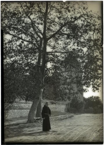 Monk standing beneath a sycamore tree at Mission Santa Barbara, Santa Barbara, circa 1898-1899