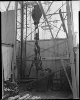 Four men standing next to the travelling block at the base of an oil well, probably at the Venice or Playa del Rey oil field, Los Angeles, circa 1930