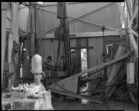 Three workers around the travelling block at an oil well, probably at the Venice or Playa del Rey oil field, Los Angeles, 1930