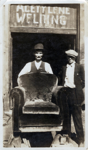 Photograph of two men standing in doorway of a welding shop