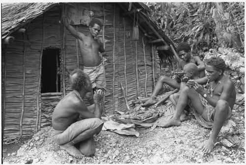 Eating ritual pork in front of men's house: the man with his hand on the house is Boofanalamo