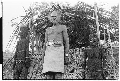 Folofo'u, wearing old police belt, on speaking platform with fernwood 'ea figures made by Arimae of Furi'ilae for the opening of the Kwaio Cultural Centre in August 1979