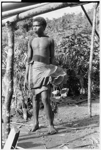 Boy by house frame, holding taro plant