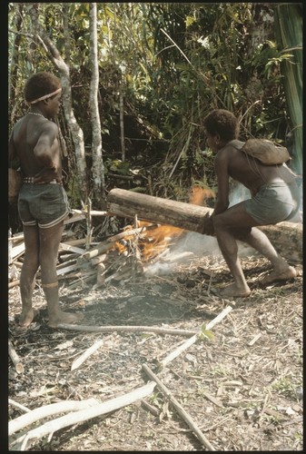 Two men heating log to remove bark