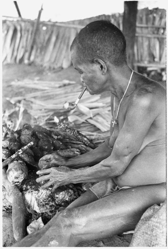 Woman wearing a cross, cooking and scraping taro on fire at Ngarinaasuru, above Sinalagu